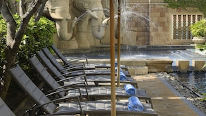 A poolside area with lounge chairs and blue umbrellas, a stone wall with a water feature, and a tiled floor. - The Great Duke Phnom Penh (Phnom Penh)