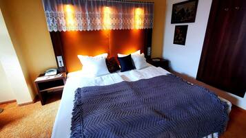 Una cama bien hecha con un edredón estampado, un teléfono en la mesita de noche y una lámpara.