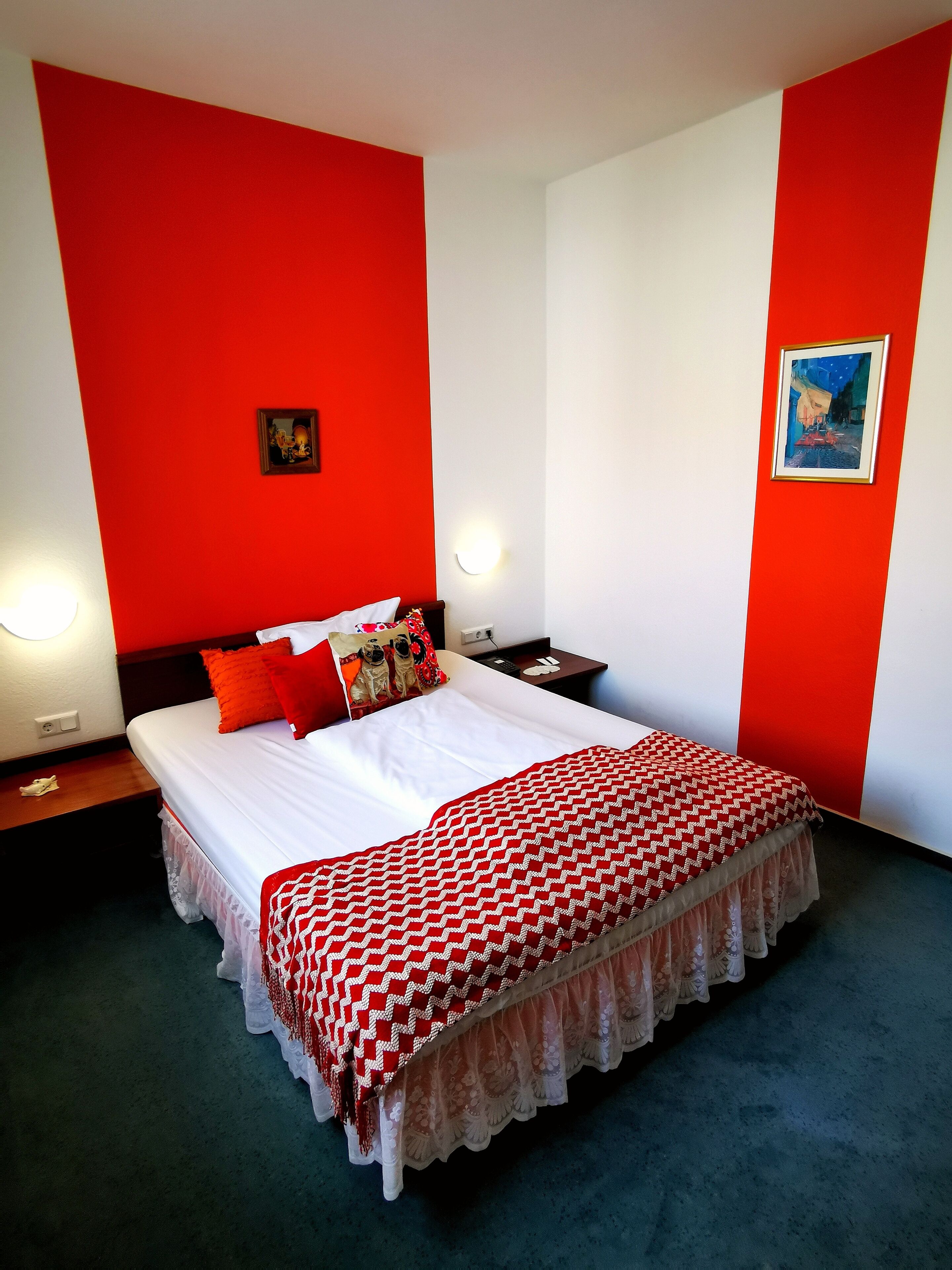 Una habitación de hotel con una cama grande, paredes rojas y blancas, un cuadro enmarcado y una mesita de noche con una lámpara.