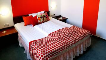 Una habitación de hotel con una cama grande, paredes rojas y blancas, un cuadro enmarcado y una mesita de noche con una lámpara.