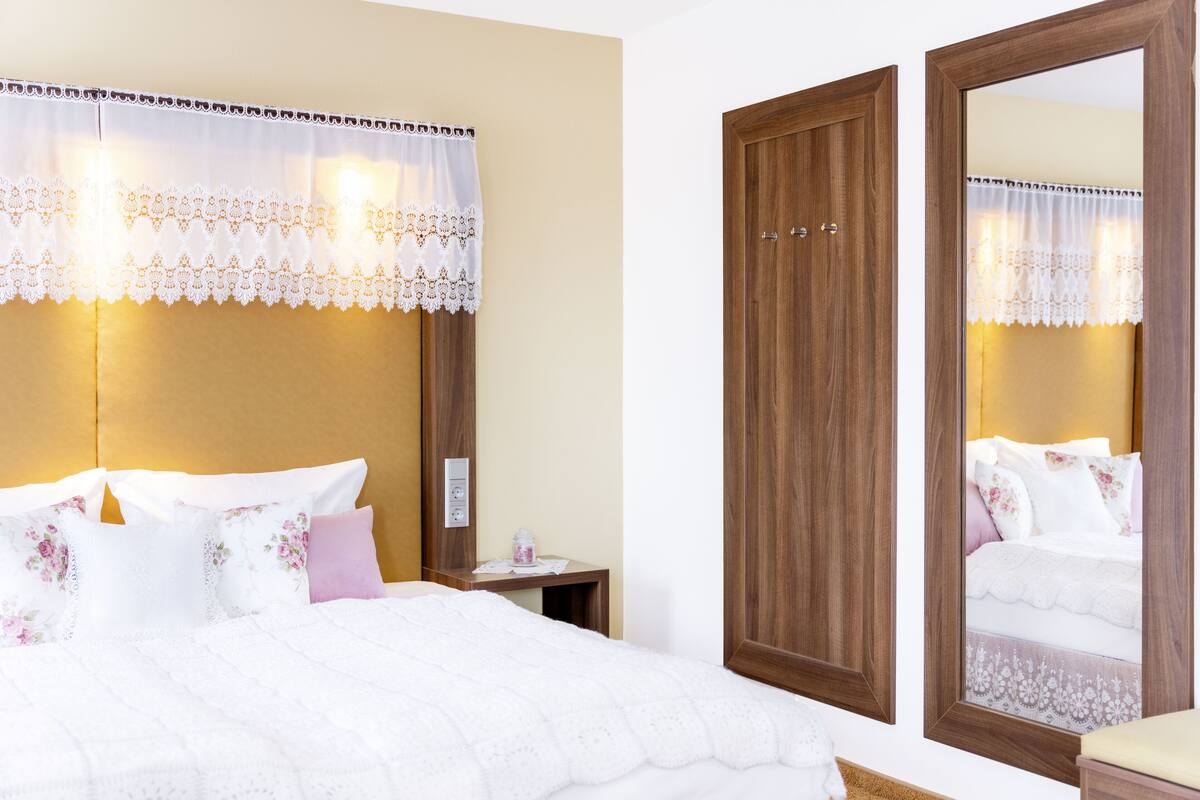 A hotel room with a large bed, a wooden wardrobe, a nightstand, and a mirror.
