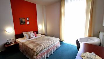 Quarto de hotel com cama, mesa de cabeceira, cadeira e vista para o exterior.