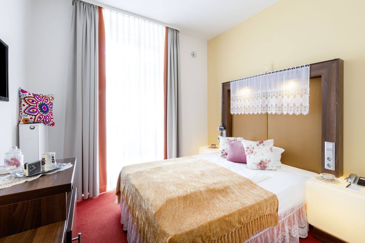 A hotel room with a bed, bedside table, lamp, and a window with curtains.