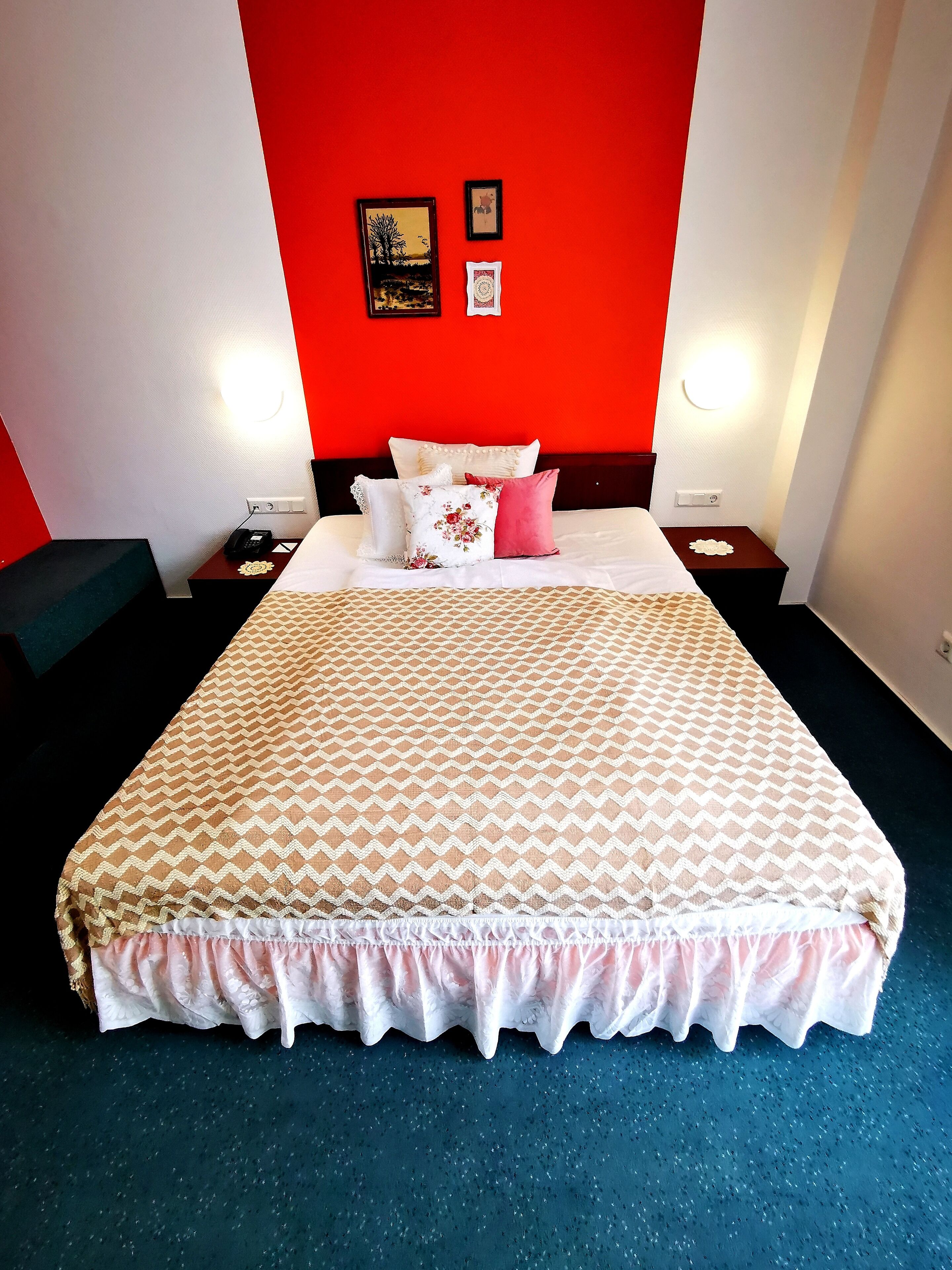 Een hotelkamer met een groot bed, twee nachtkastjes, een rode accentmuur en twee ingelijste foto's.