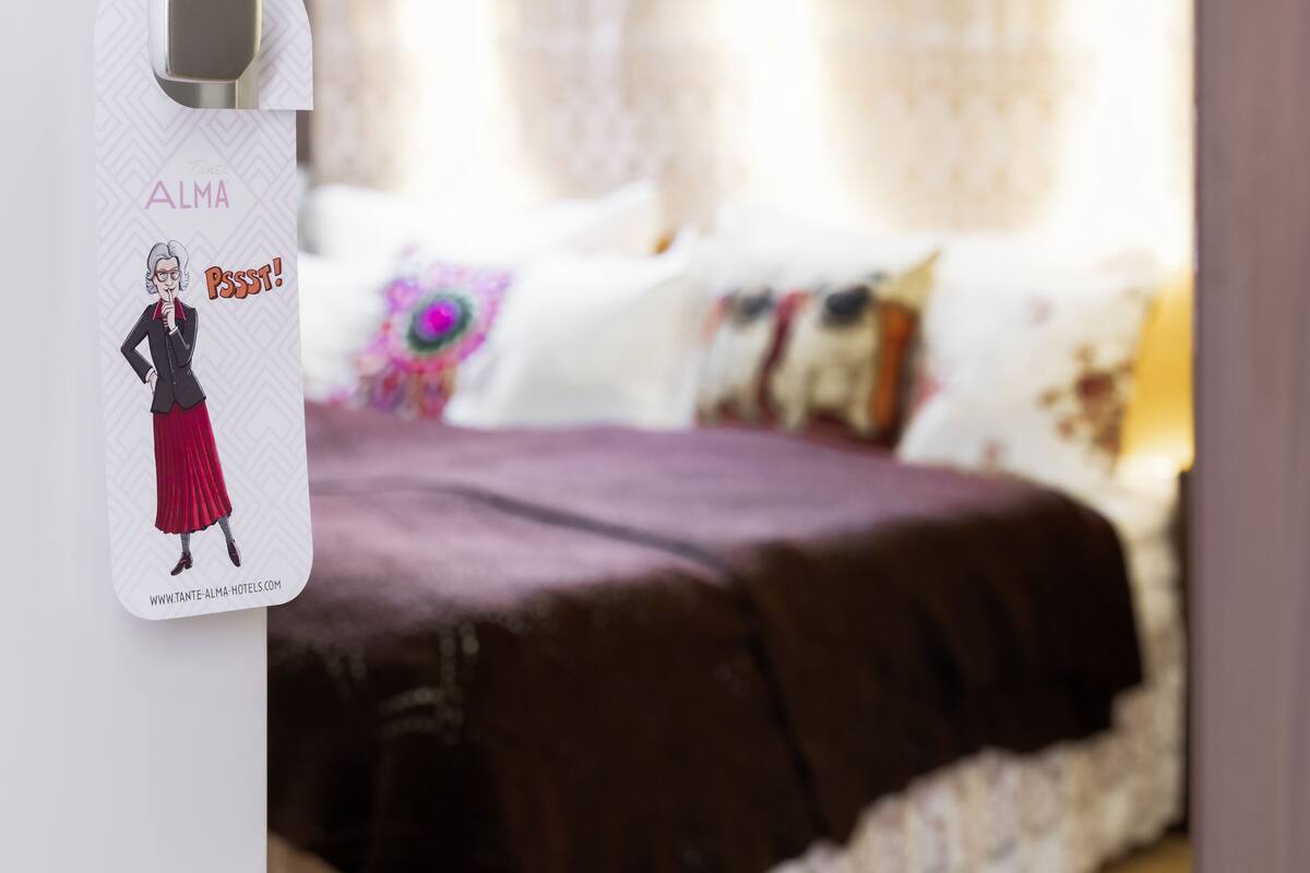 A bedroom with a bed, a window with curtains, and a wall-mounted item with a drawing and text.