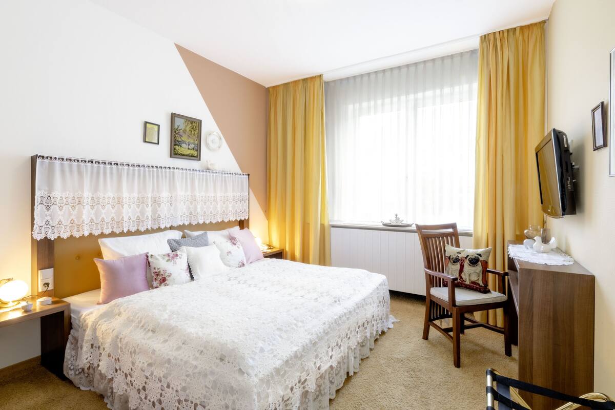 A hotel room with a large bed, a desk, a chair, a television, and a window with curtains.