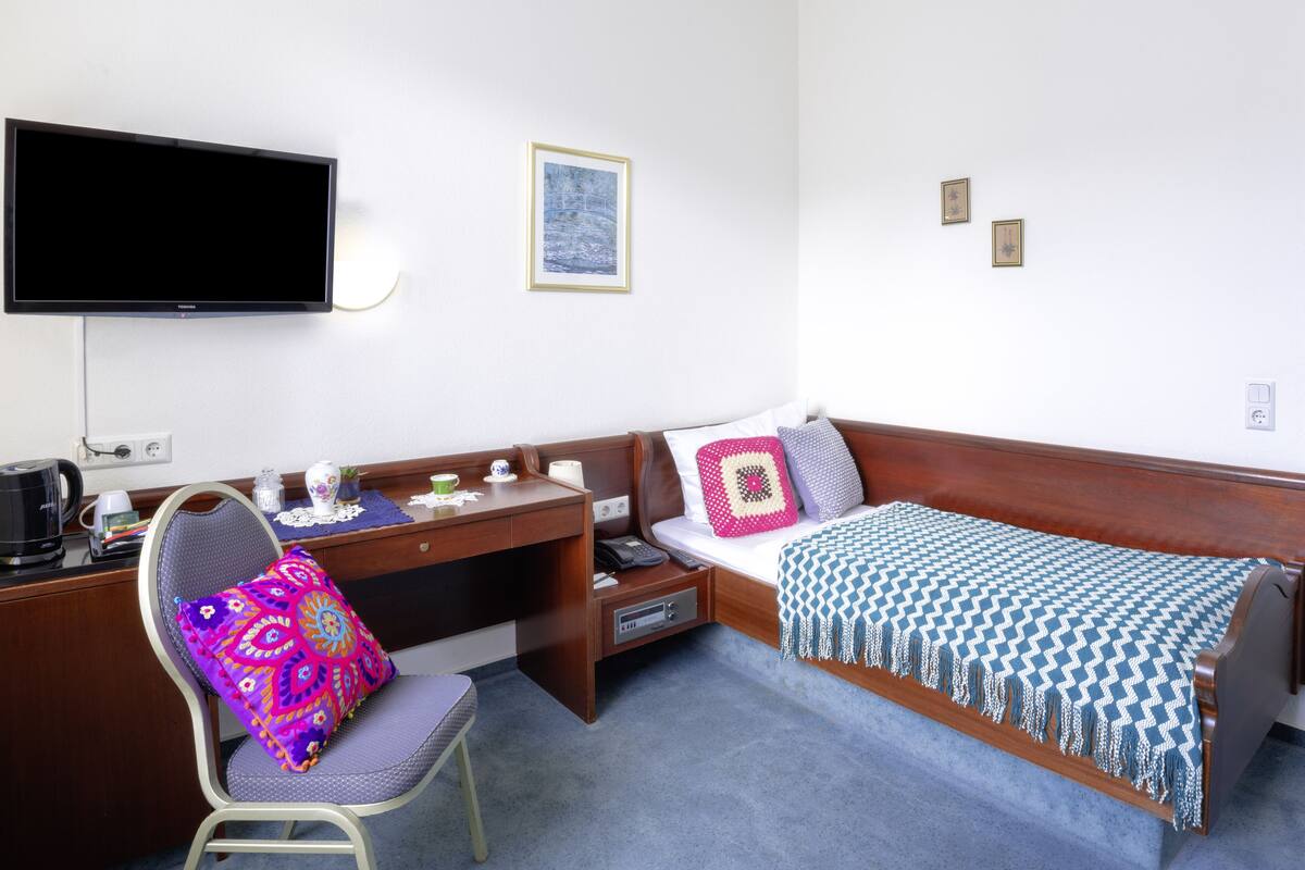 A hotel room with a bed, a desk, a chair, a television, and a small table with a coffee maker and cups.