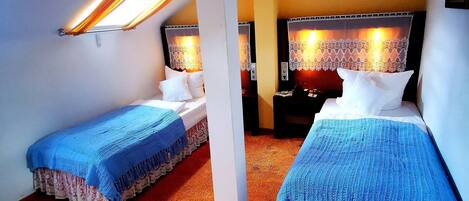 A room with two beds, a ceiling fan, and a nightstand with a lamp.