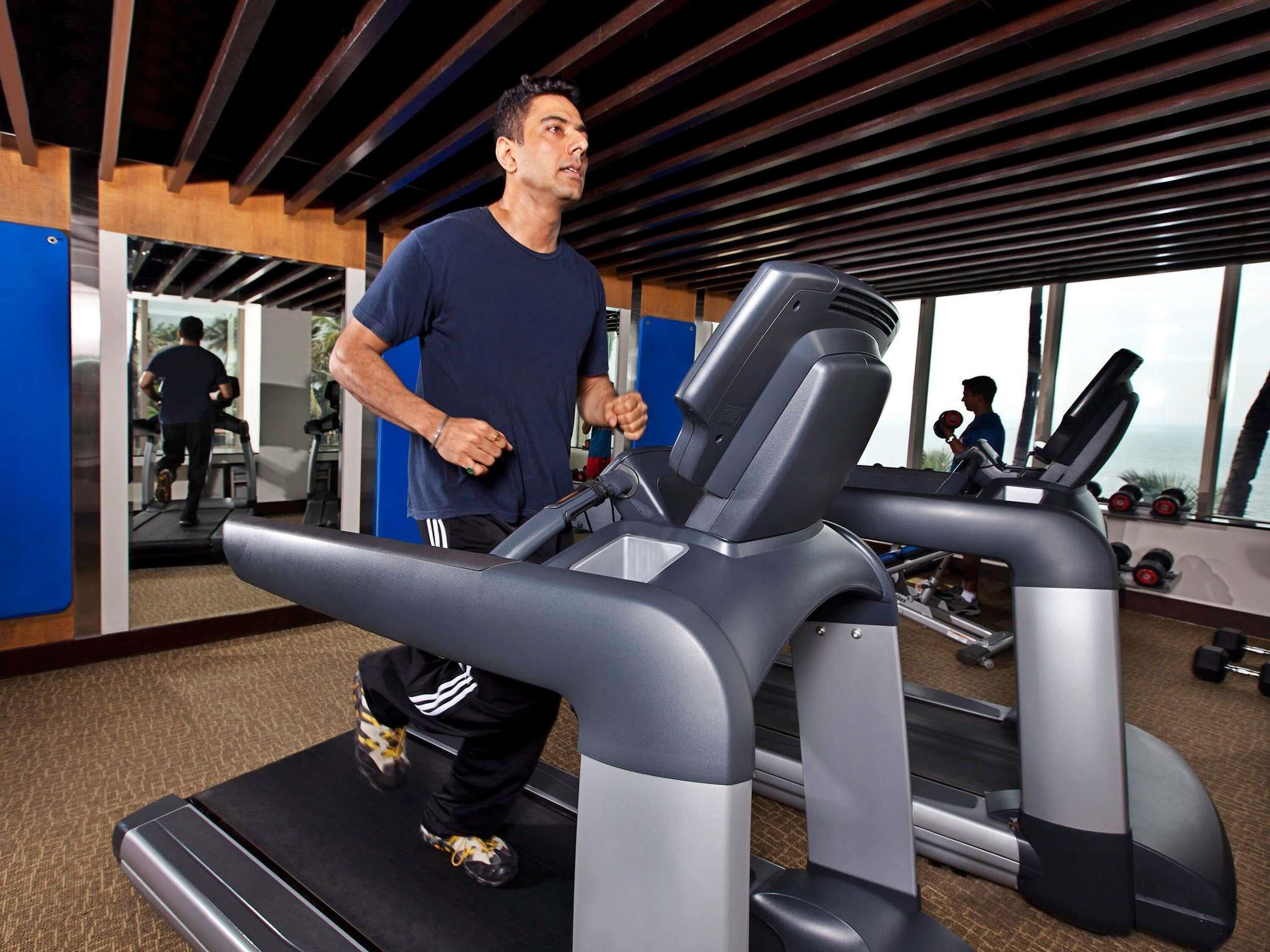 A man running on a treadmill in a gym with exercise equipment and a large window.