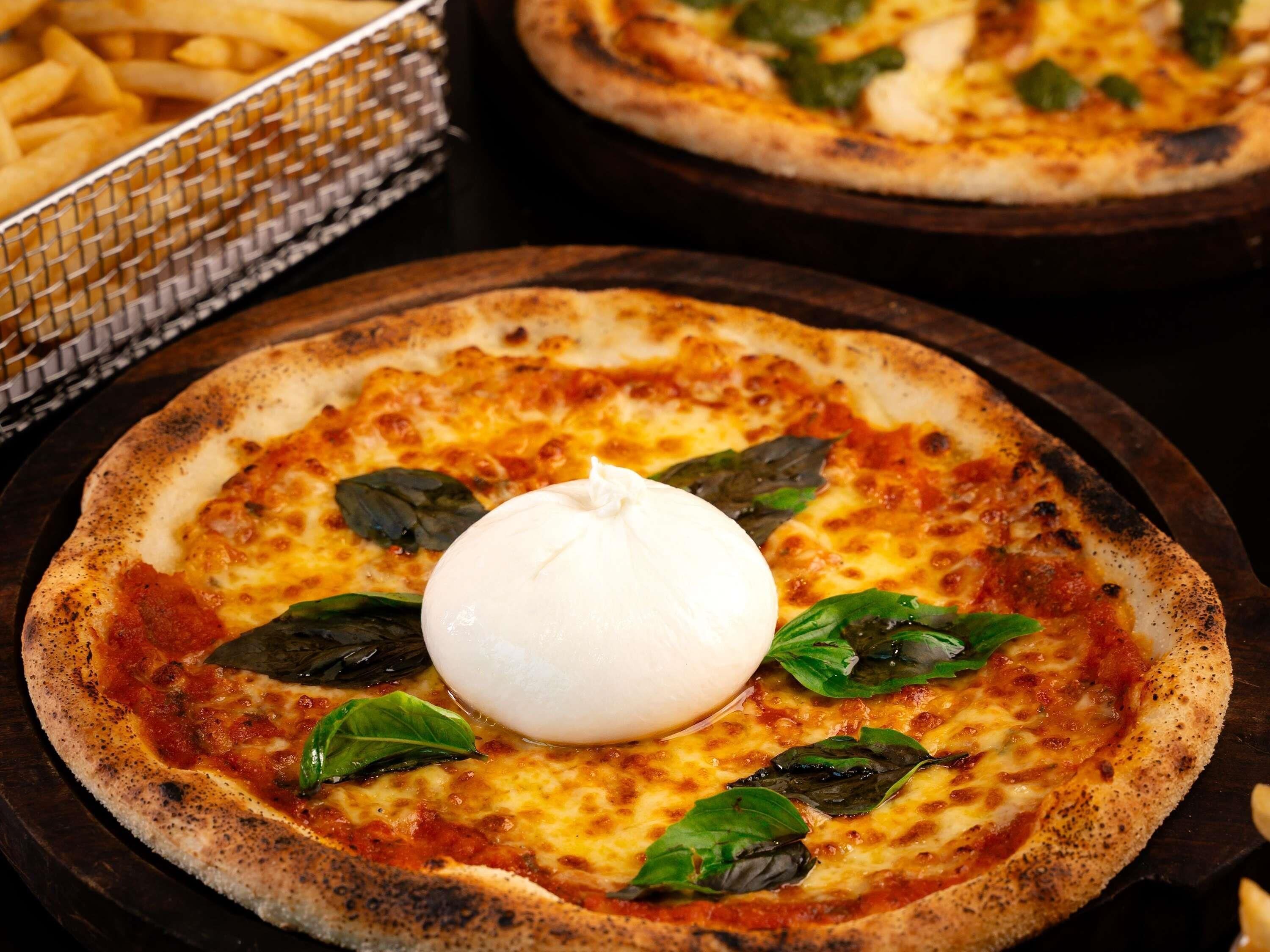 Une pizza garnie d’une cuillerée de crème et de feuilles de basilic, présentée sur une planche en bois.