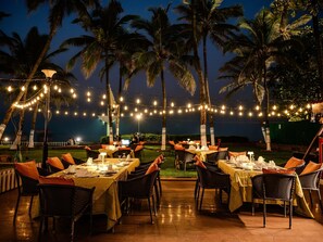 An outdoor dining area with tables set for two, string lights overhead, and palm trees in the background. - Novotel Mumbai Juhu Beach Hotel (Mumbai)