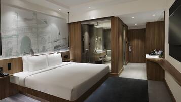 A modern hotel room with a large bed, a bathroom with a glass shower enclosure, and a wall-mounted TV.