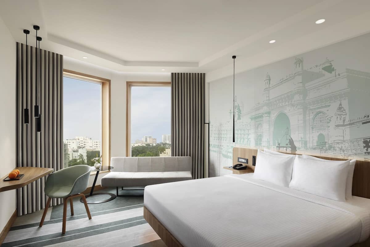 Una habitació d'hotel amb un llit gran, un escriptori, una cadira, vista a la ciutat i un mural a la paret.