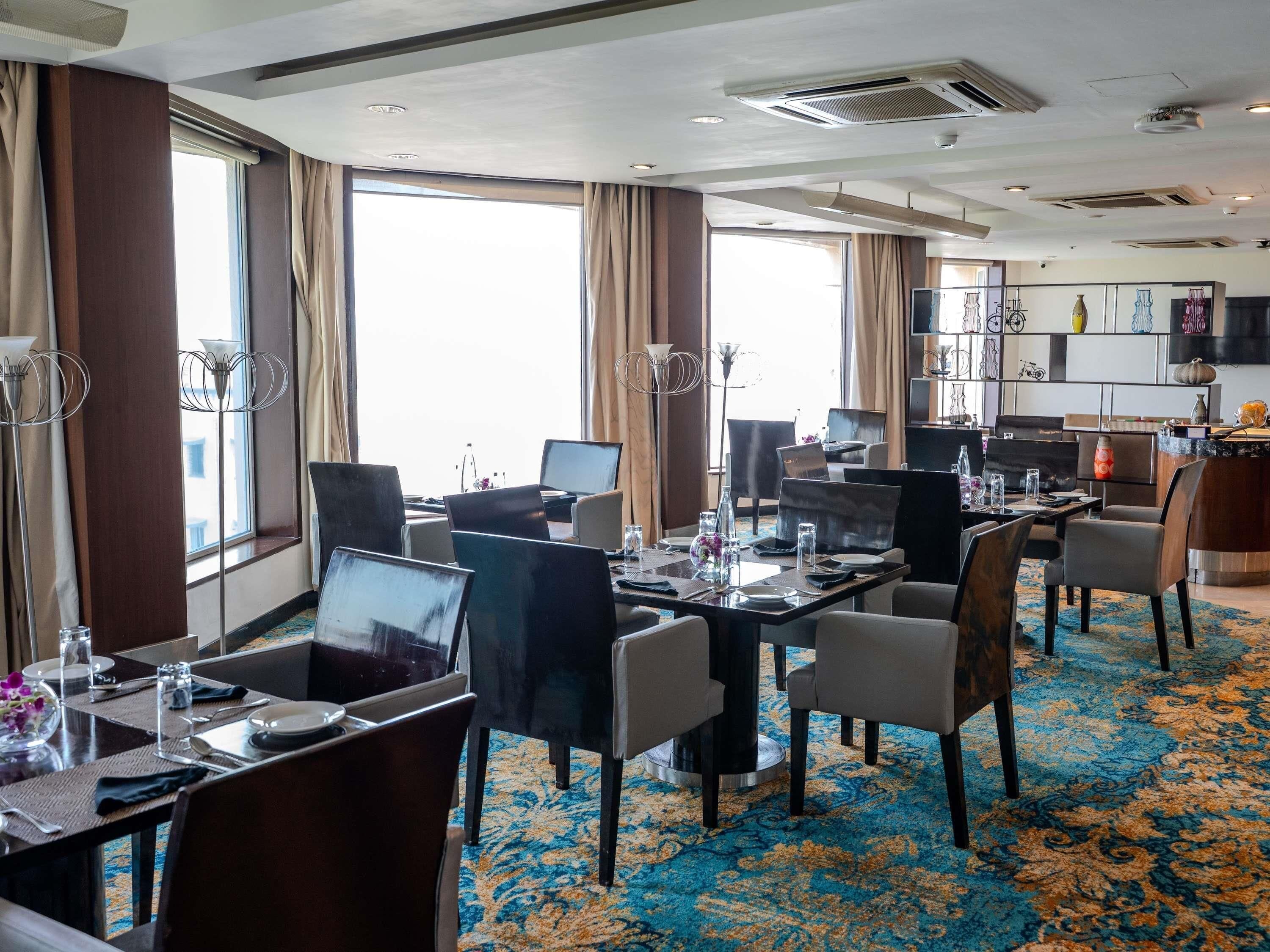 A hotel conference room with multiple tables, chairs, and a large window providing a view.