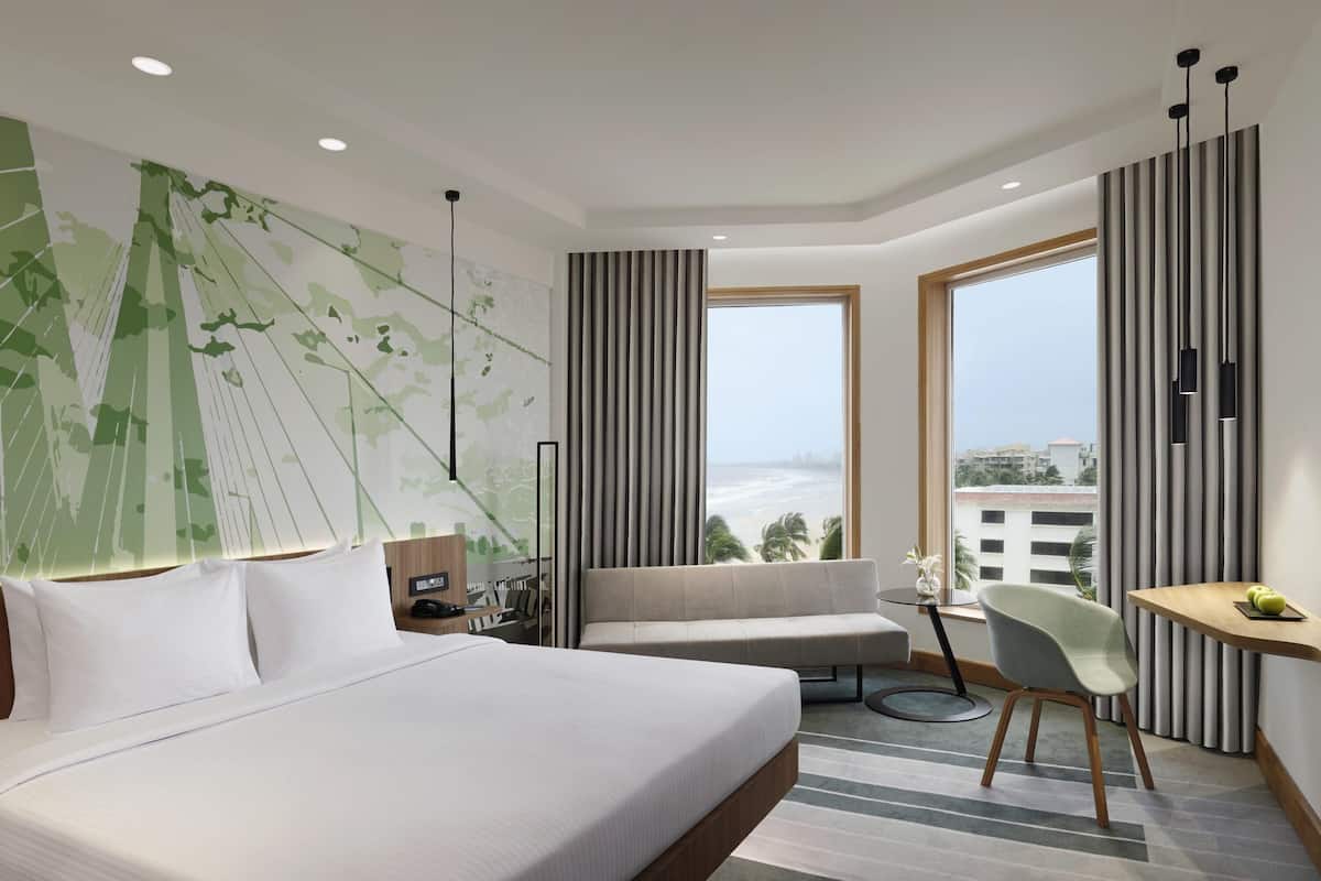 Habitació d'hotel moderna amb un llit gran, un sofà, una taula de treball i vistes a la platja.