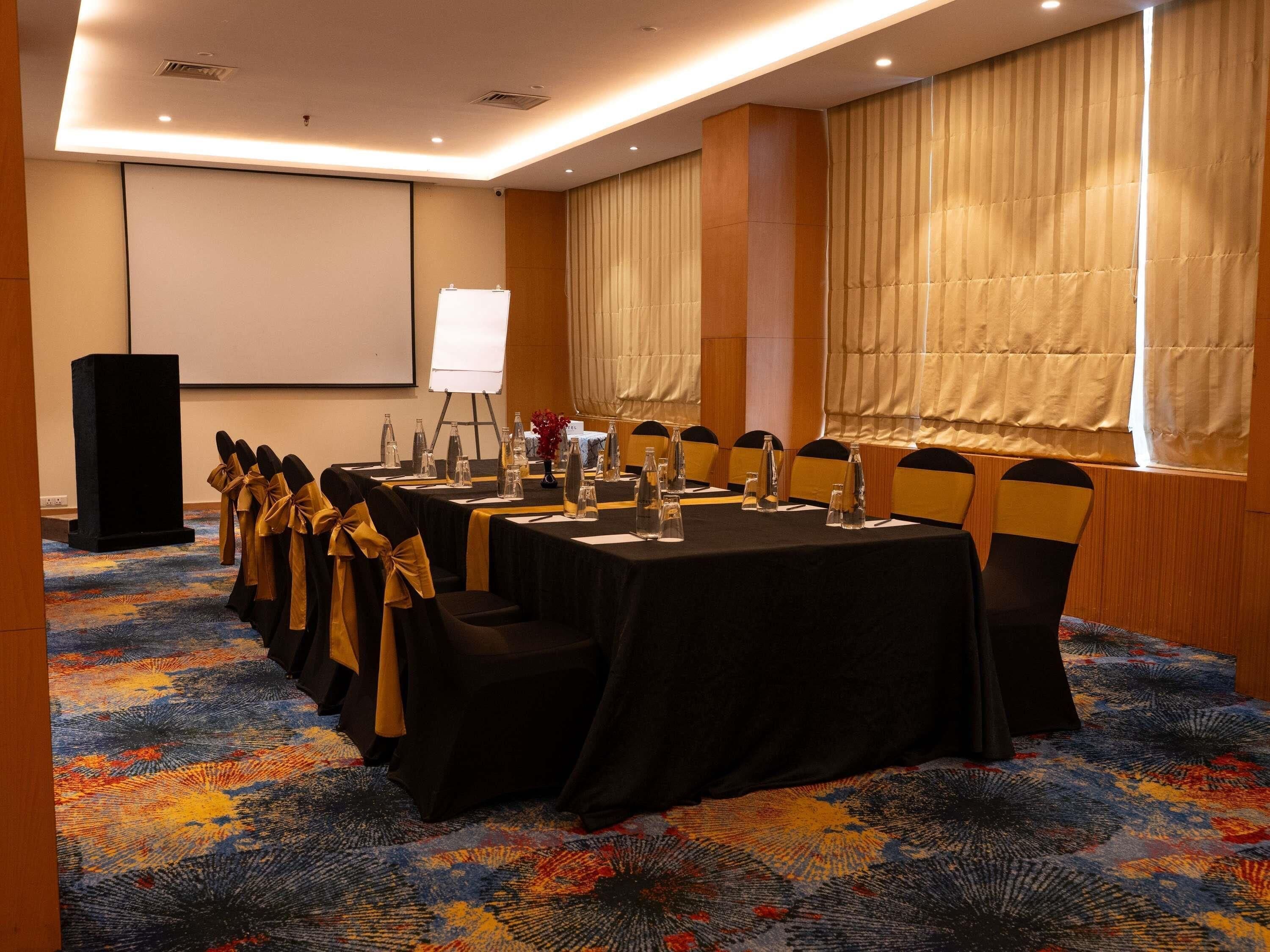 A conference room with a long table, chairs, a podium, and a projector screen.
