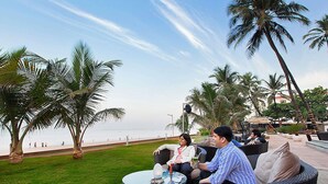 Eine Terrasse mit Korbmöbeln, einem Glastisch und Blick auf den Strand und Palmen.