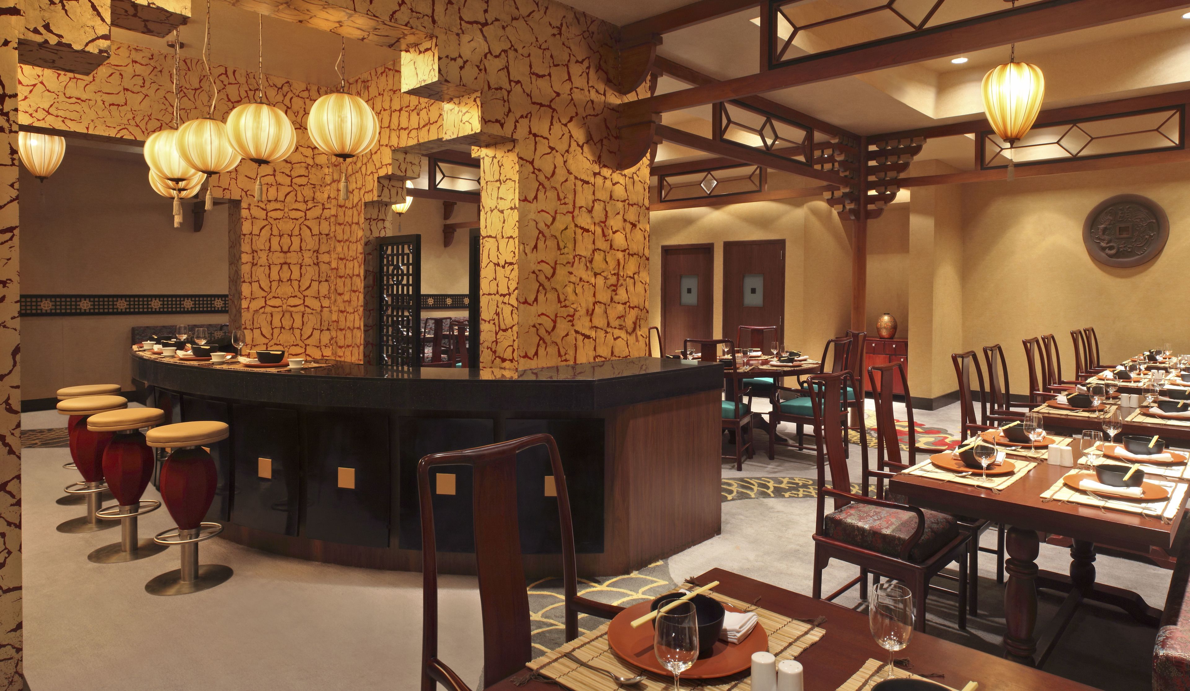 A restaurant with a central bar, multiple dining tables, and red bar stools.