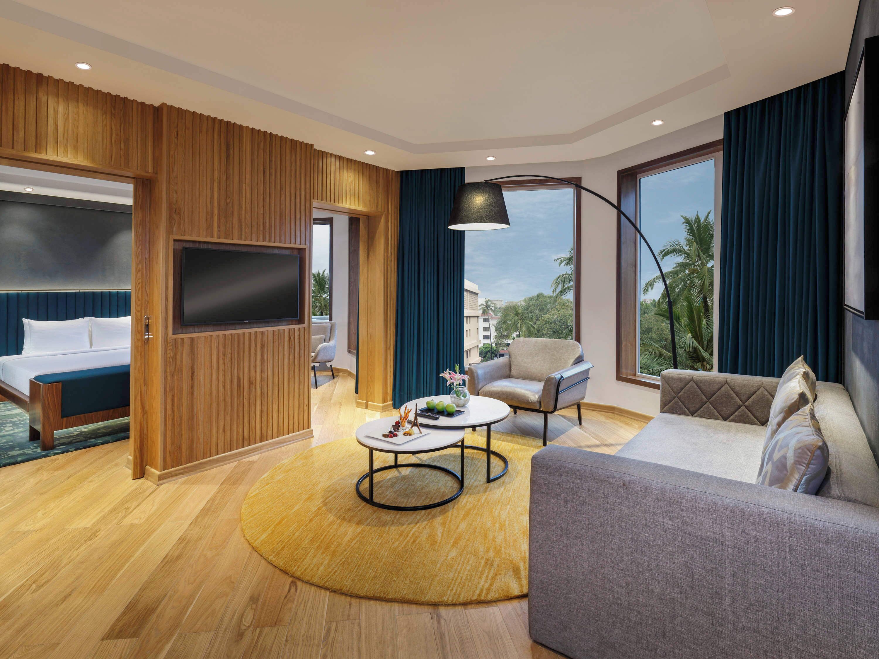 A modern hotel room with a bed, a sofa, a coffee table, and a TV.