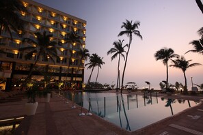 Ein Hotel mit Pool, Palmen und Sonnenuntergang.