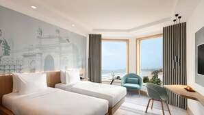 Une chambre d’hôtel avec deux lits, un bureau, une chaise, une télévision et une grande fenêtre donnant sur la plage.