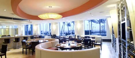 A modern dining area with a central seating arrangement, large windows, and a ceiling with circular design elements.