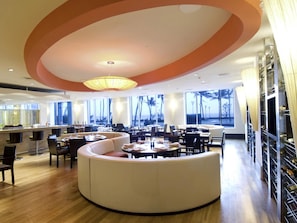 A modern restaurant with a central seating area, large windows, and a curved ceiling design. - Novotel Mumbai Juhu Beach Hotel (Mumbai)