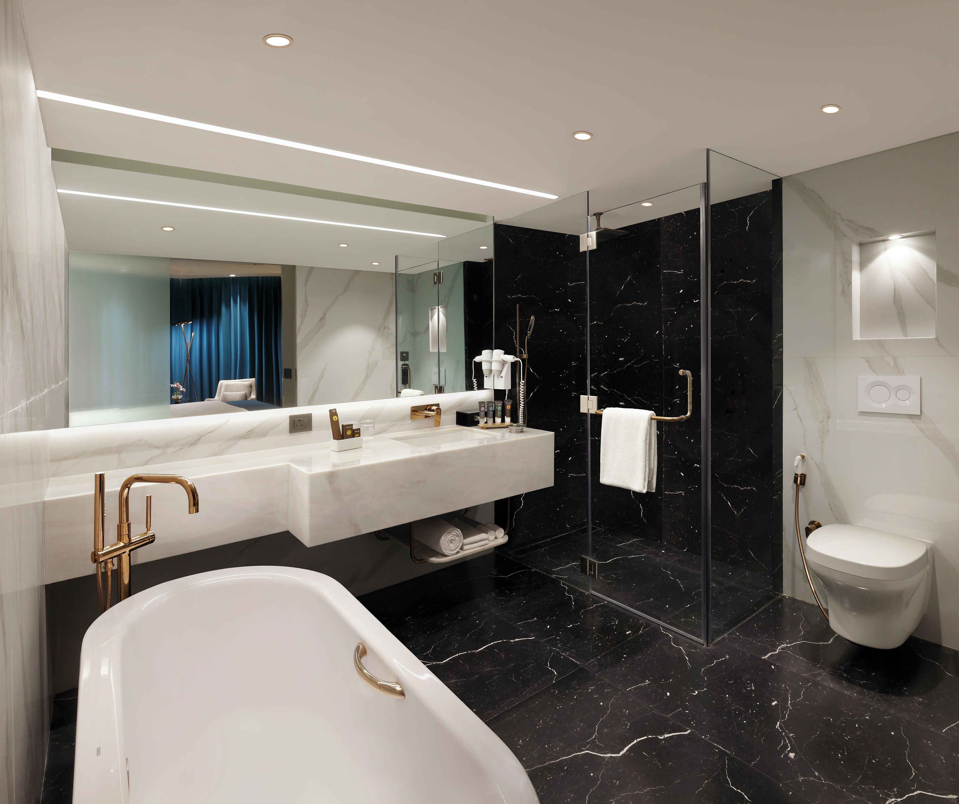 A modern bathroom with a large mirror, a bathtub, a shower, and a toilet.