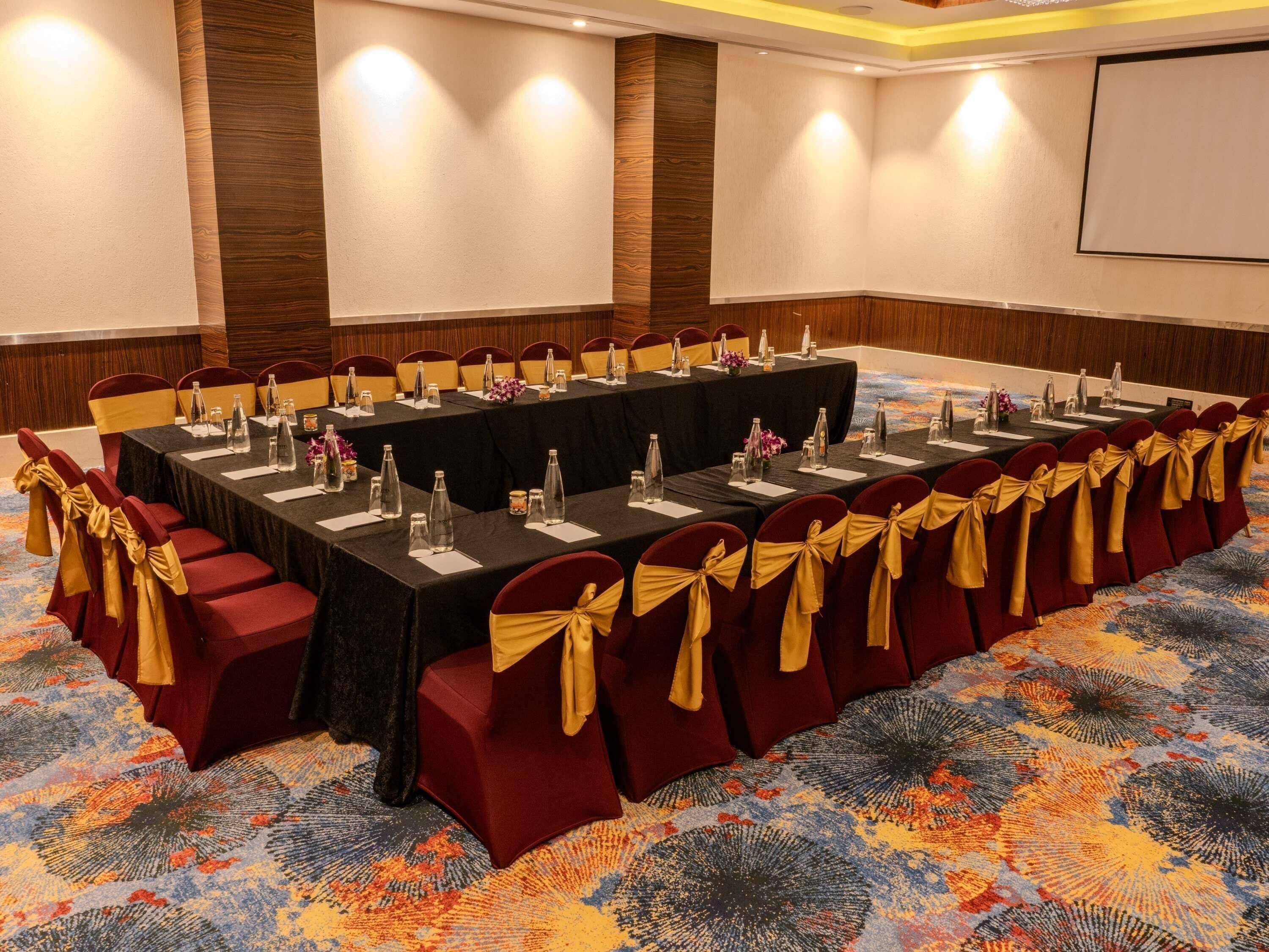 A conference room with a long table, red chairs with gold sashes, and a carpeted floor.