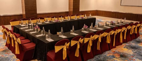 A conference room with a long table, red chairs with gold sashes, and a carpeted floor.