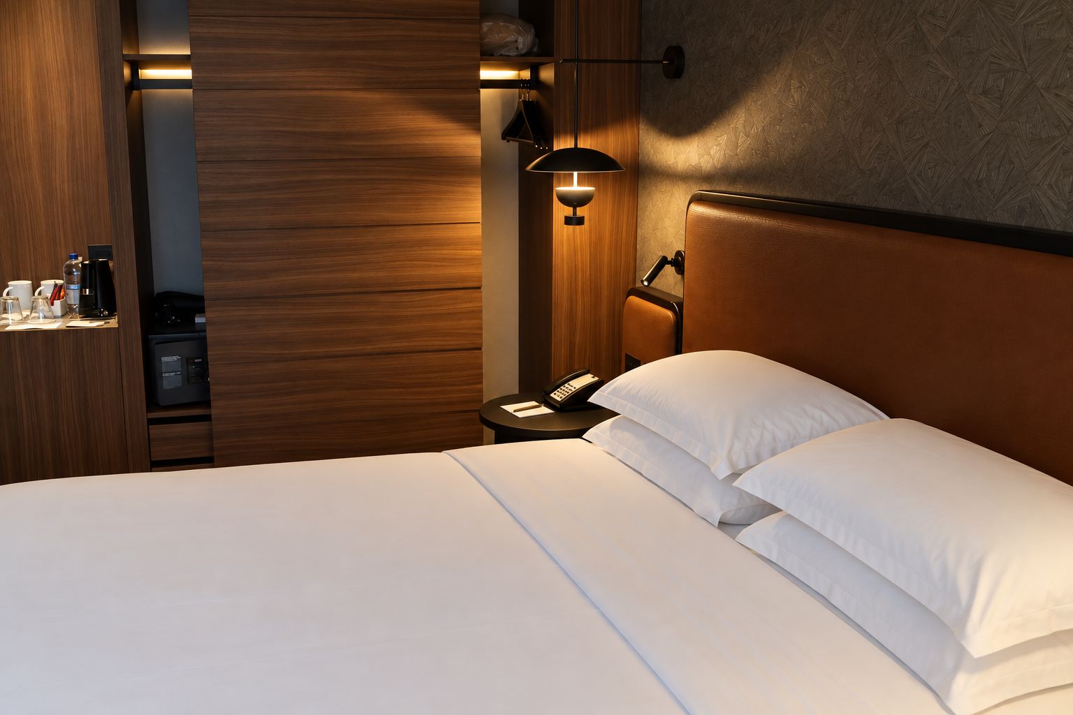Habitación de hotel con cama, mesita de noche, lámpara y teléfono fijo en la pared.