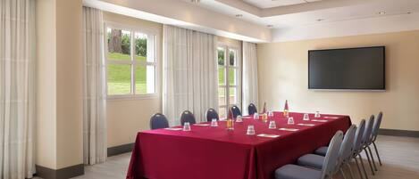 A conference room with a long table, chairs, a projector screen, and windows with curtains.