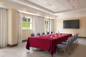 A conference room with a long table, chairs, a projector screen, and windows with curtains. - Sheraton Rome Parco de’ Medici (Rome)