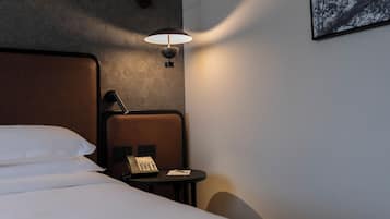 Ett hotellrum med en säng, ett sängbord med en telefon, en lampa och en tavla som hänger på väggen.