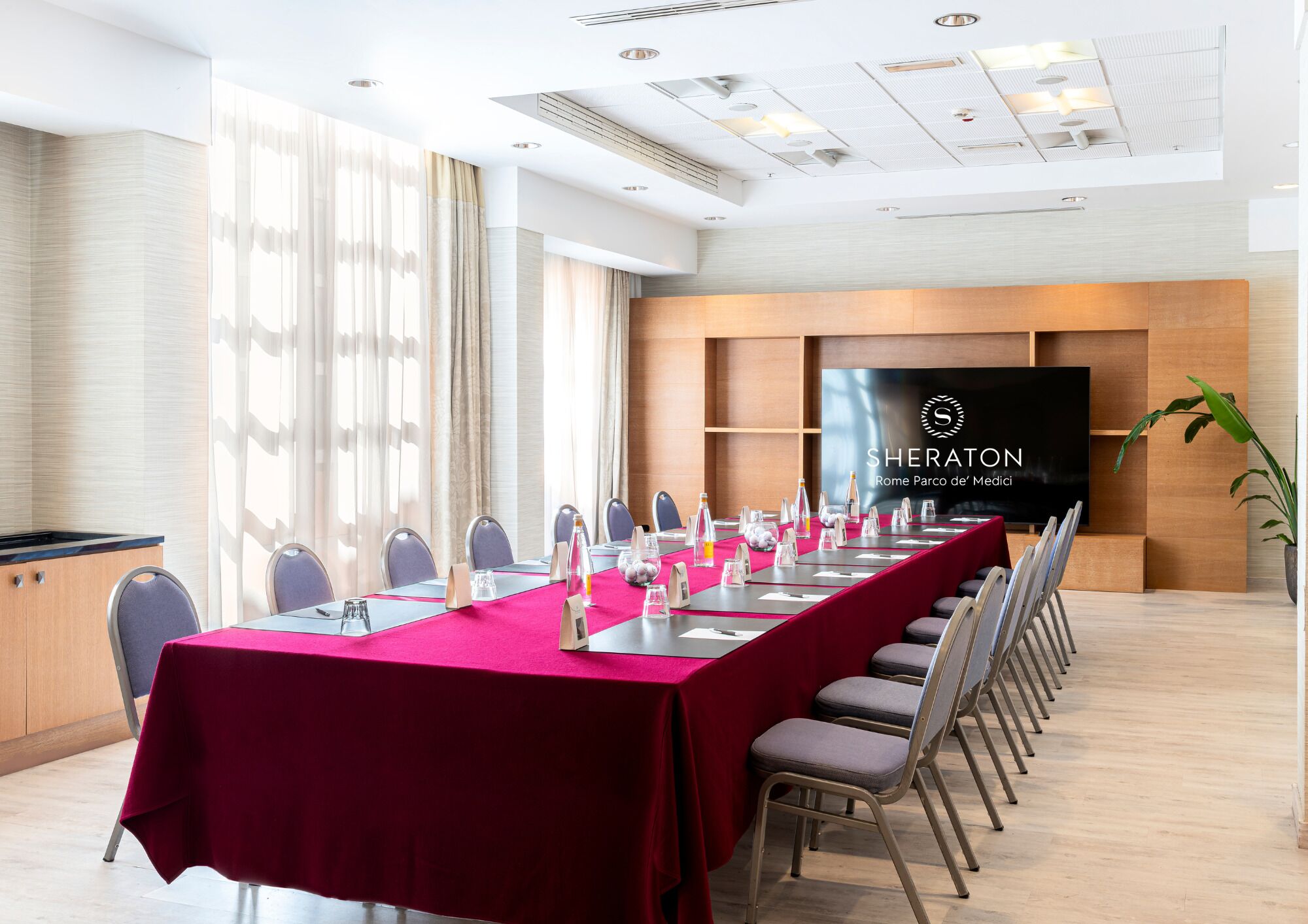 Uma sala de conferência com uma mesa comprida, cadeiras e uma tela grande exibindo o logotipo Sheraton.