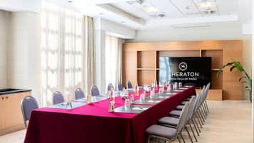 Uma sala de conferência com uma mesa comprida, cadeiras e uma tela grande exibindo o logotipo Sheraton.