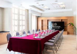 A conference room with a long table, chairs, and a large screen displaying the Sheraton logo. - Sheraton Rome Parco de’ Medici (Rome)