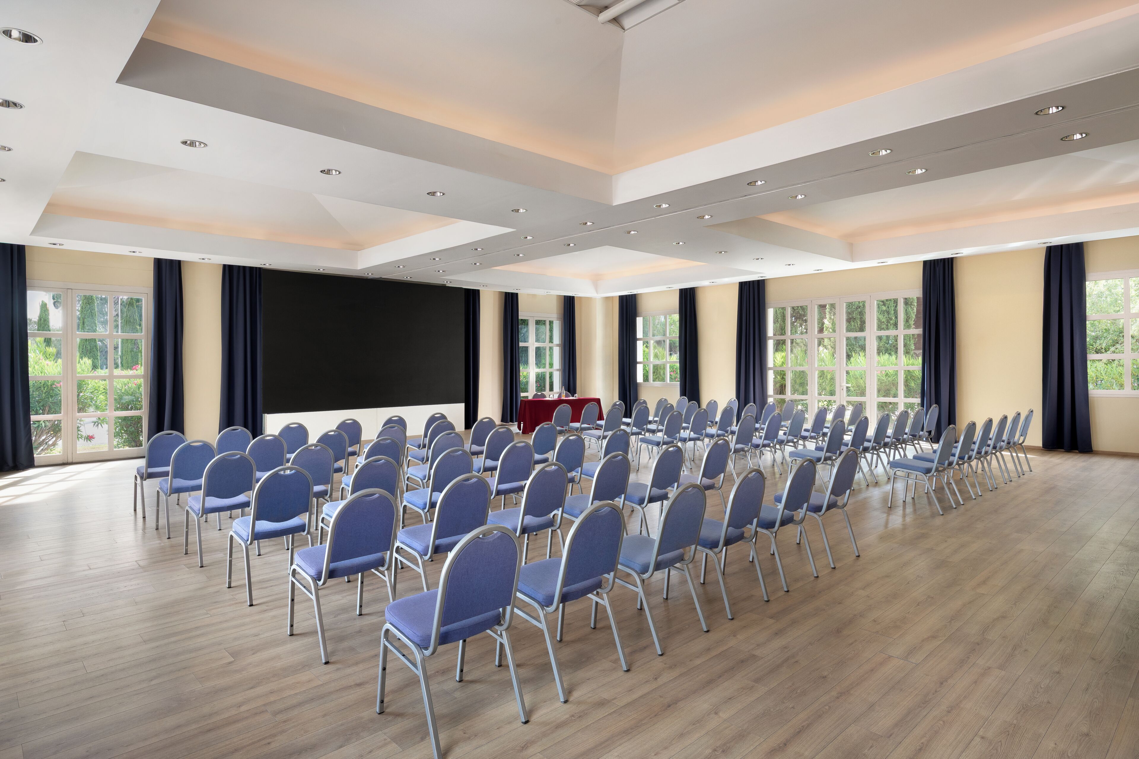 A conference room with rows of chairs, a large screen, and windows with curtains.