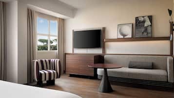 A hotel room with a bed, a seating area with a sofa and armchair, a television, and a small table.