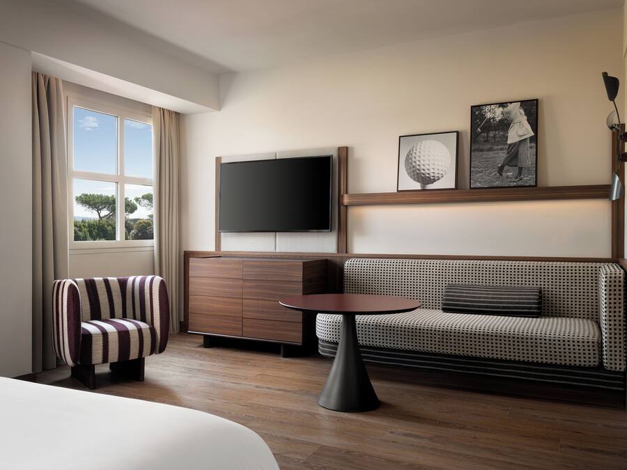 A hotel room with a bed, a seating area with a sofa and armchair, a television, and a small table.