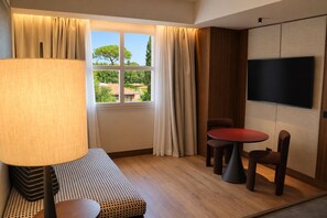 Ein Hotelzimmer mit Sofa, einem kleinen Tisch, einem Fernseher und einem Fenster mit Vorhängen.