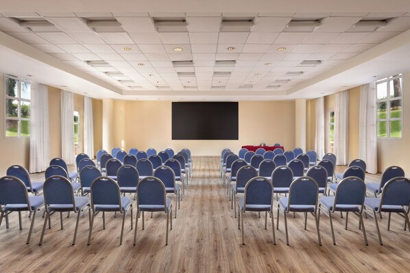 A conference room with rows of chairs, a large screen, and windows.