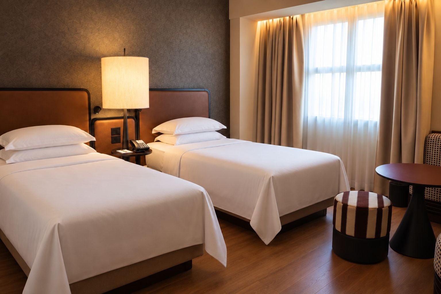 Une chambre d’hôtel avec deux lits, une table de chevet avec une lampe, un téléphone et une petite table ronde avec une chaise.