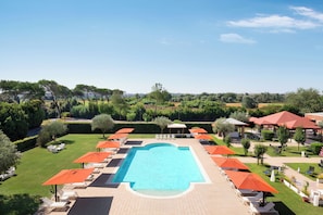 A swimming pool with surrounding lounge chairs and umbrellas, set in a landscaped garden with trees and a clear sky. - Sheraton Rome Parco de’ Medici (Rome)