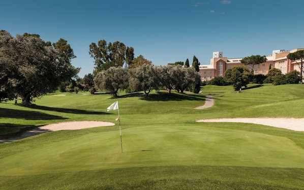 A golf course with bunkers, a flag, and a building in the background.