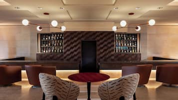 Zona de bar con una pantalla central, dos sillones estampados y estantes llenos de botellas.