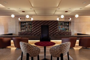 A bar area with a central TV screen, two patterned chairs, and shelves of bottles.