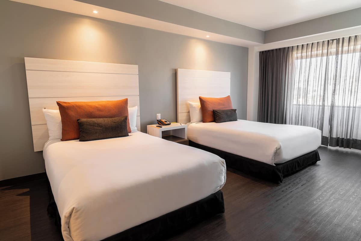 A hotel room with two beds, each with a headboard, a nightstand, and a telephone.