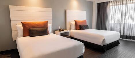 A hotel room with two beds, each with a headboard, a nightstand, and a telephone.