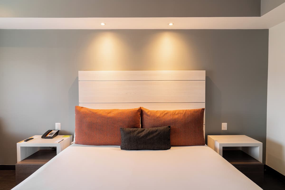 A modern hotel room with a large bed, two nightstands, and a headboard with built-in lighting.